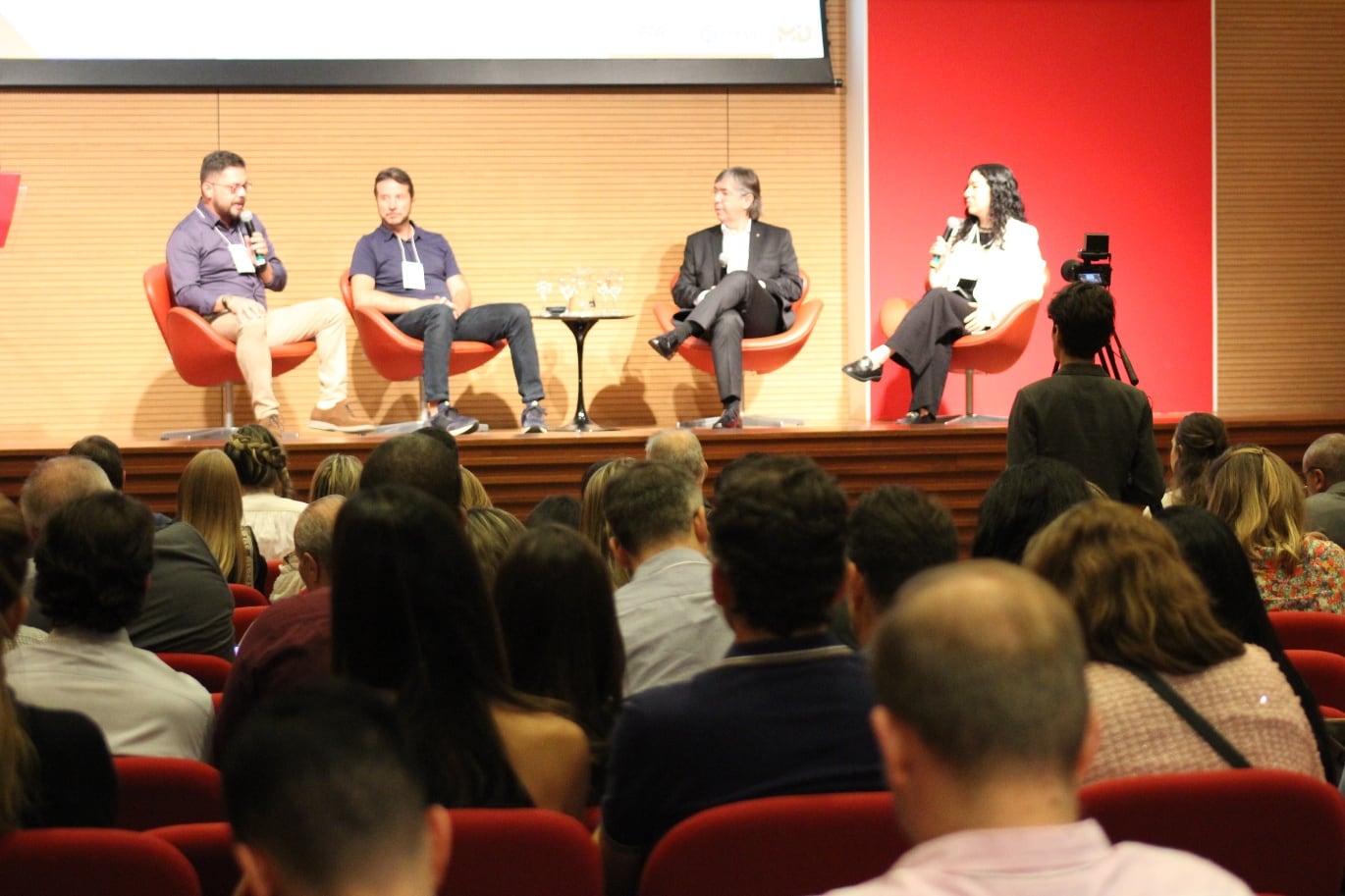 Painel no palco visto da plateia, com o auditório cheio